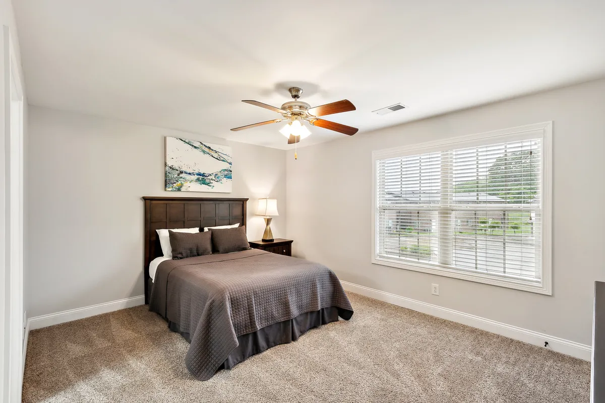 A serene bedroom scene featuring a bed with a gray comforter, an art piece above the headboard, and a window with blinds letting in natural morning light. The overall mood is cozy, calm, and inviting, evoking a sense of retreat and relaxation after a day of adventure.