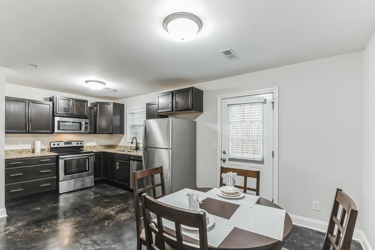 A spacious dining area adjacent to the kitchen, featuring a dining table set for a family meal, granite countertops, and modern appliances in the background. The setup emphasizes togetherness, hospitality, and the ease of entertaining guests.