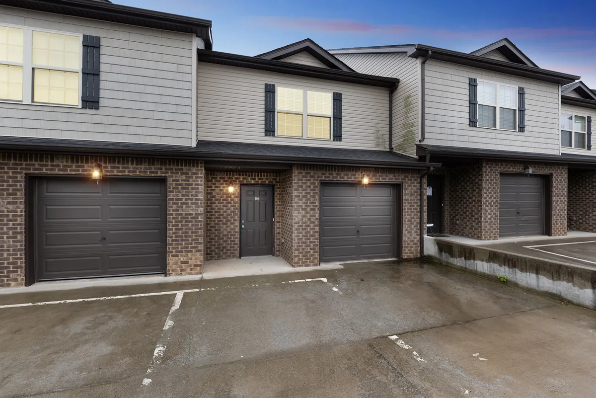 A wider exterior perspective of the townhouse-style facade, featuring multiple garage doors, large windows, and a prominent front door. The scene suggests a sense of community and ease, while highlighting the architectural style and the spacious parking arrangement.