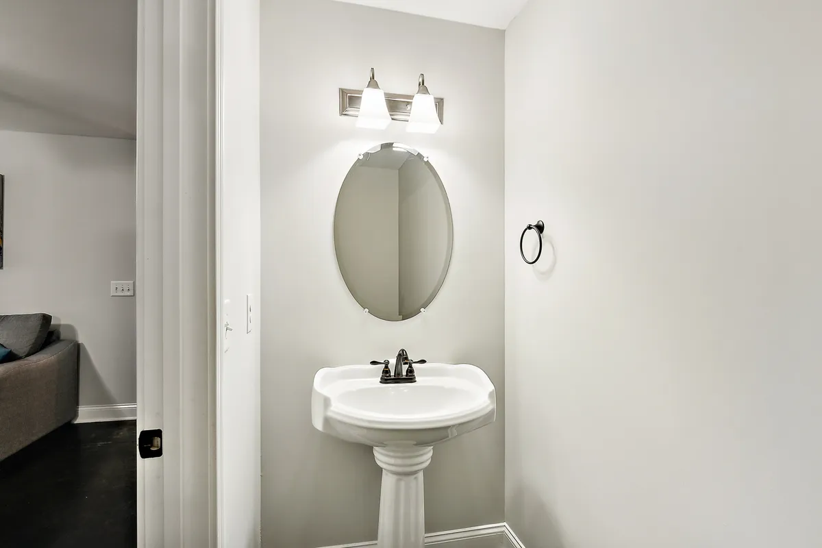 A bright, inviting bathroom featuring a pedestal sink, oval mirror, and stylish lighting fixtures. The space is functional and designed for quick touch-ups or moments of self-care while getting ready for a day or night out.