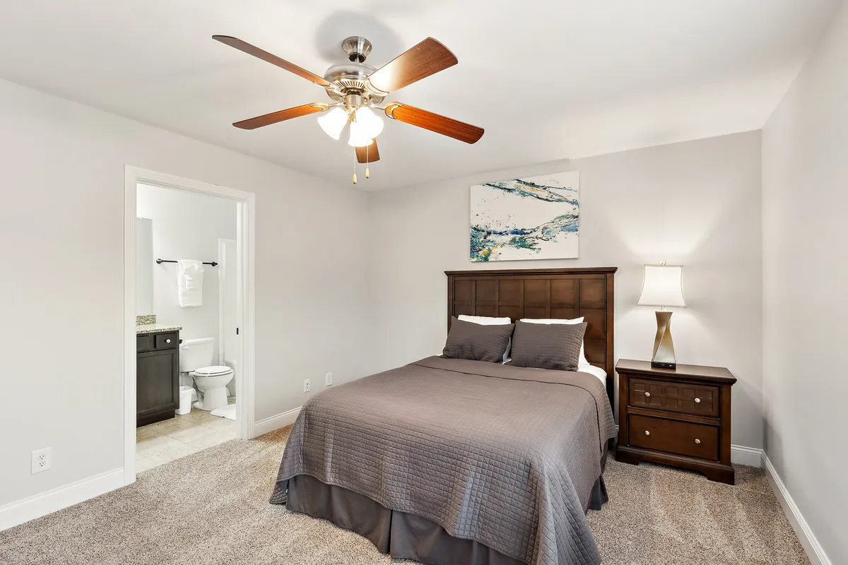 A serene bedroom featuring a stylish bed with soft gray bedding, a modern nightstand topped with a glowing lamp, and tasteful wall art, creating a cozy and inviting atmosphere.