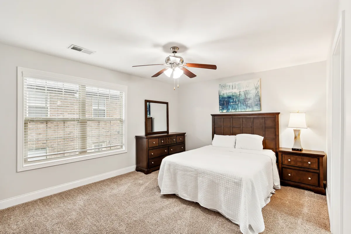 A bright and inviting bedroom featuring a bed with crisp white bedding, a wooden dresser, a mirror, and tasteful artwork on the wall. The room is bathed in natural light, highlighting the fresh linens and comfortable furnishings.