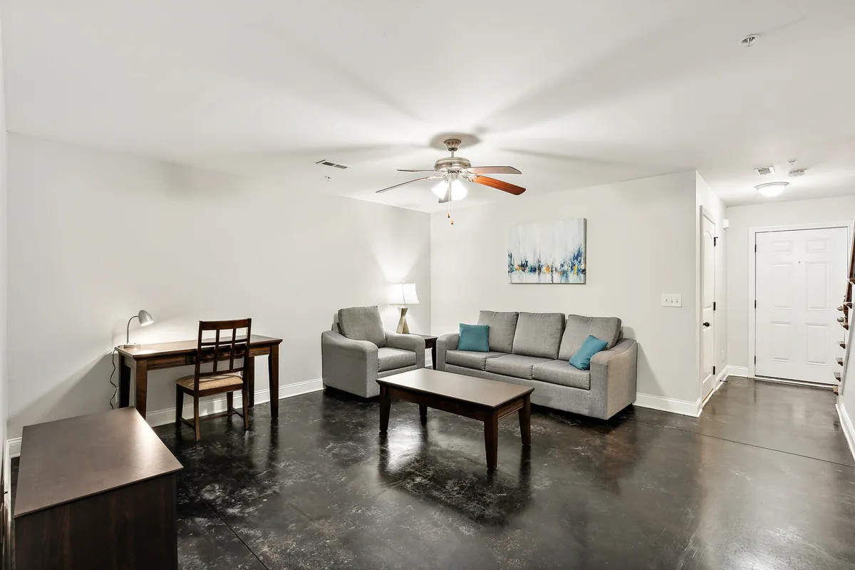 A comfortable living area showcasing a stylish sofa, a practical desk, a coffee table, and decorative artwork, all arranged to foster relaxation, socializing, and productive work sessions. Warm lighting adds to the cozy, welcoming ambiance.
